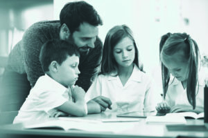 Male Primary teacher with three students working in class